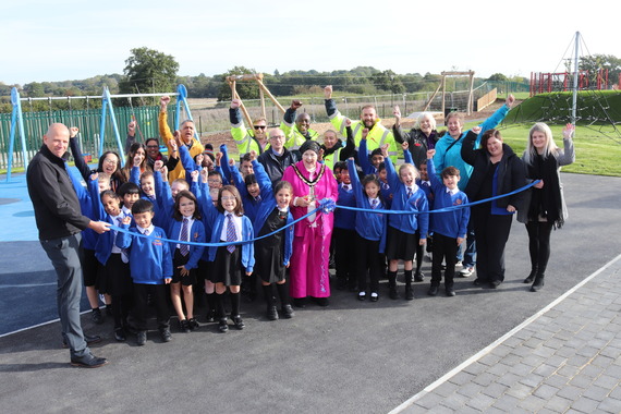 A large group of children and adults cheer as the Mayor of the borough opens a new playground by cutting a ribbon