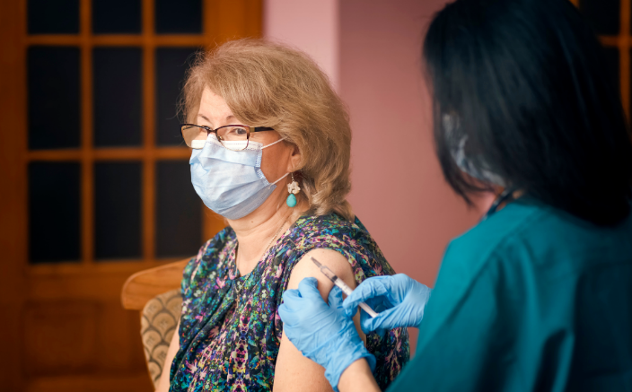 A woman in a face mask is given a vaccine in her left arm