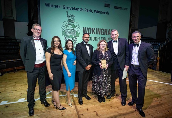 a group of men and women in formal evening wear collect an award with the Wokingham Borough Council logo projected on a screen behind them