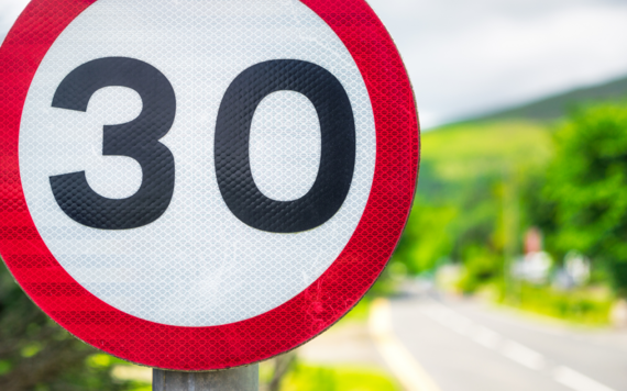 Close up of a 30mph speed sign, blurred road and greenery can be seen in the background