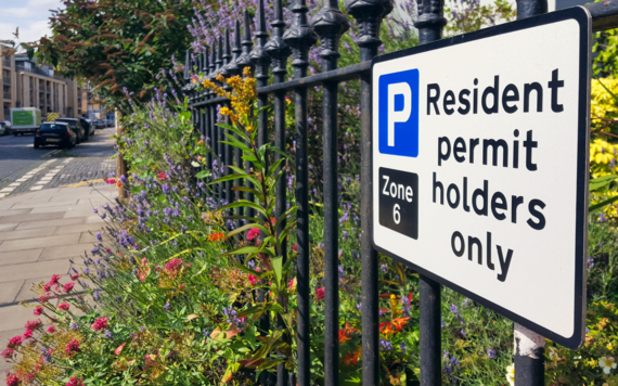 A sign reading residents parking only on an iron railed fence surrounded by wildflowers