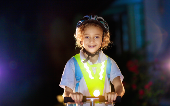 A girl wearing a school uniform and helmet on a scooter wearing reflective vest