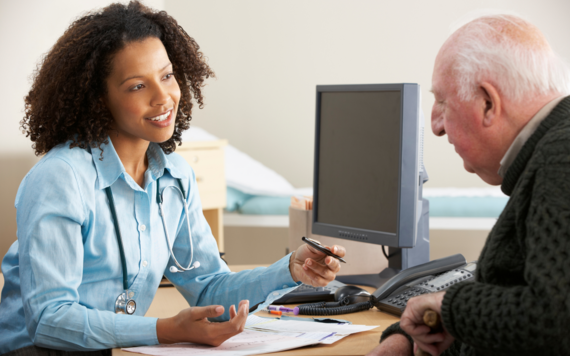 Medical professional at a desk talking to an older man