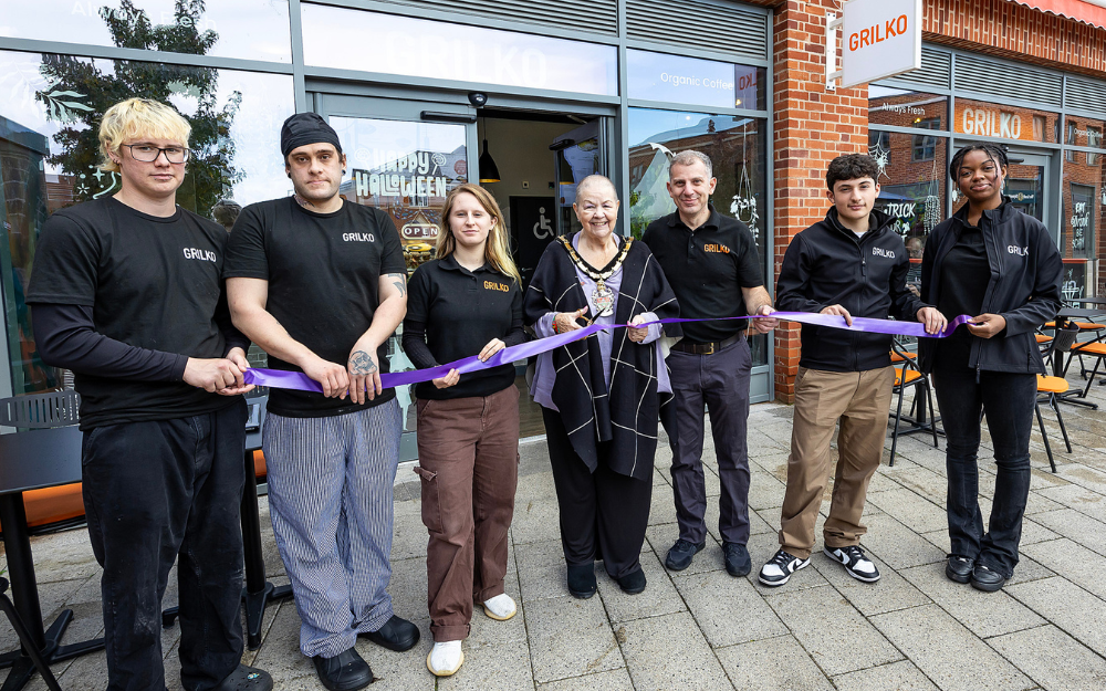 A group of people stand outside an attractive modern shop unit, preparing to cut a ribbon