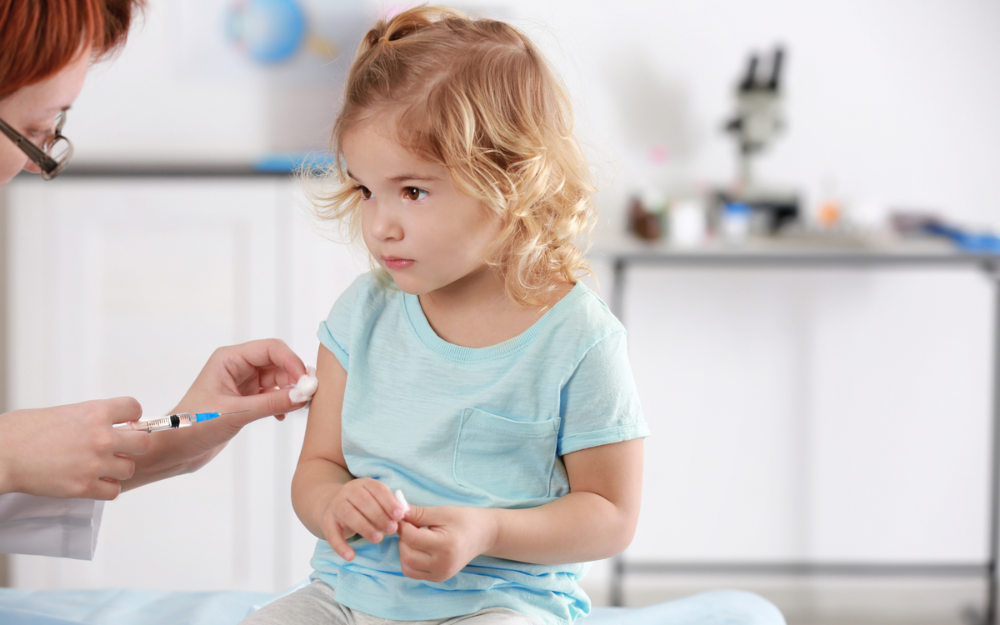 A young child sits calmly as she gets ready to get a vaccine