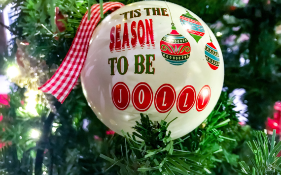 A close-up of a bauble on a Christmas tree that read 'tis the season to be jolly