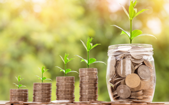 A few stacks of coins and a jar of coins, all with a plant growing on top