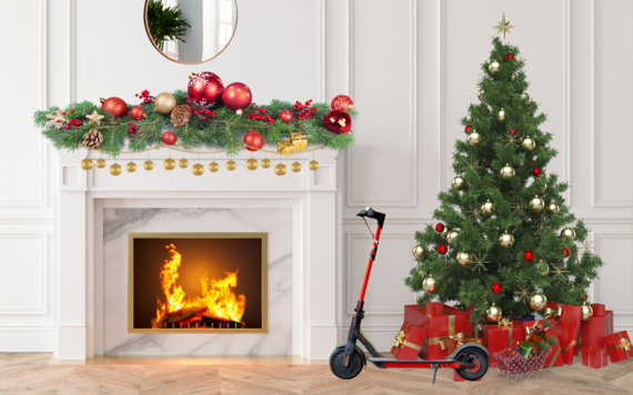 A Christmas tree next to a lit fireplace, with wrapped presents and an e-scooter underneath