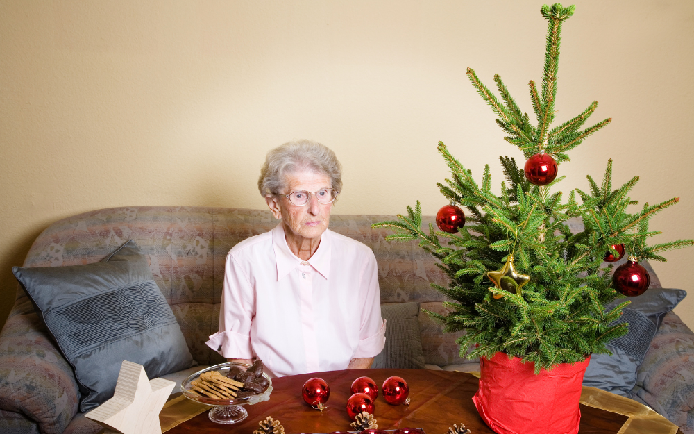 A woman sat on a sofa with small plate of festive food and Christmas tree