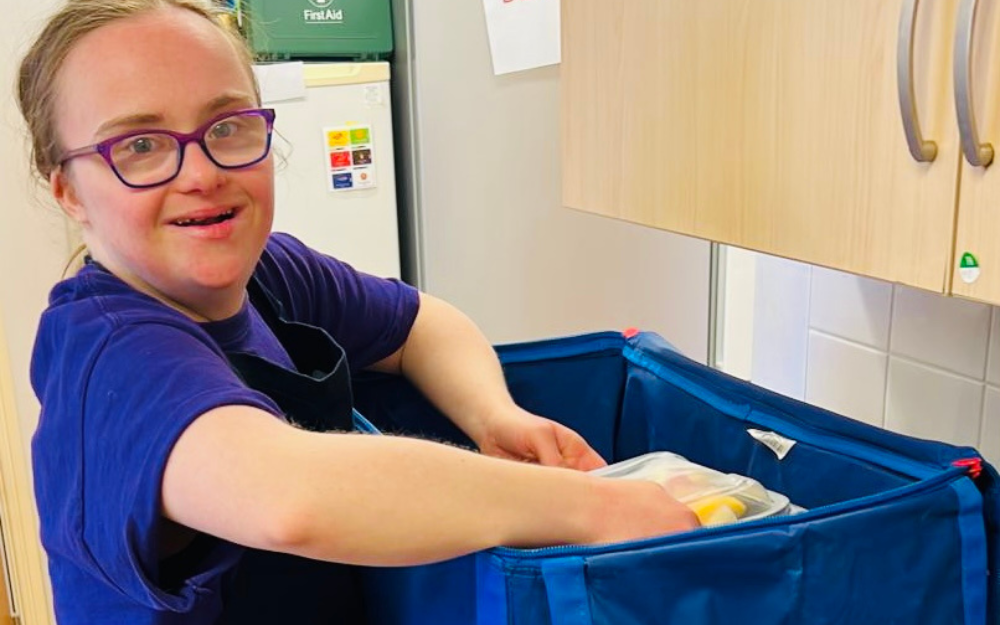 An adult with learning disabilities at work smiles to the camera