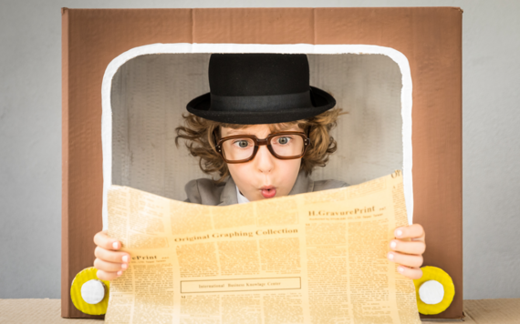 A child wearing a bowler hat and tweed jacket in old fashioned television frame holding newspaper out looking surprised