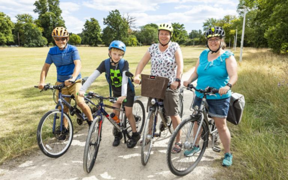 Three adults and a child sitting on bicycles on a bike path smiling at the camera