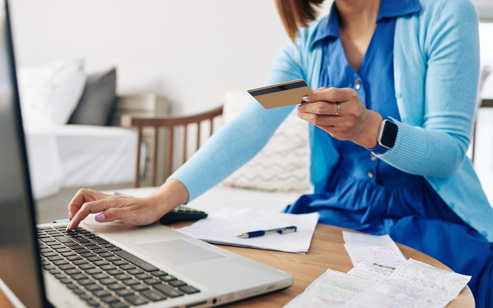 A woman at a laptop with her finances in front of her, including a bank card