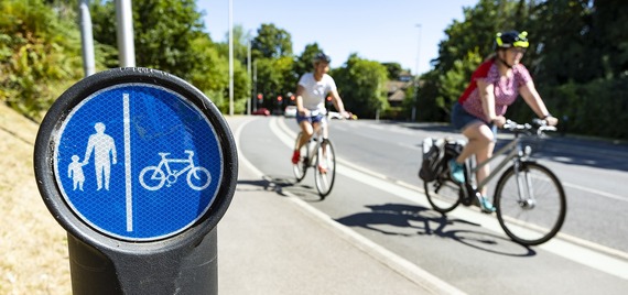 two woman ride bicycles along a shared footway and cycle way in the background, with bollard and cycleway sign in foreground