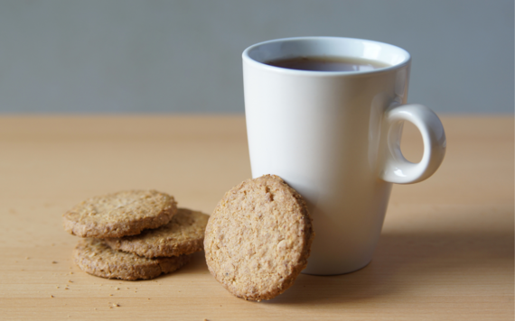 A white mug of tea, with four brown oat biscuits stacked next to it