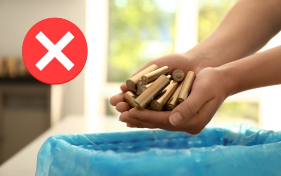 A close-up of hands putting batteries into a bin. A symbol of a cross in top left corner
