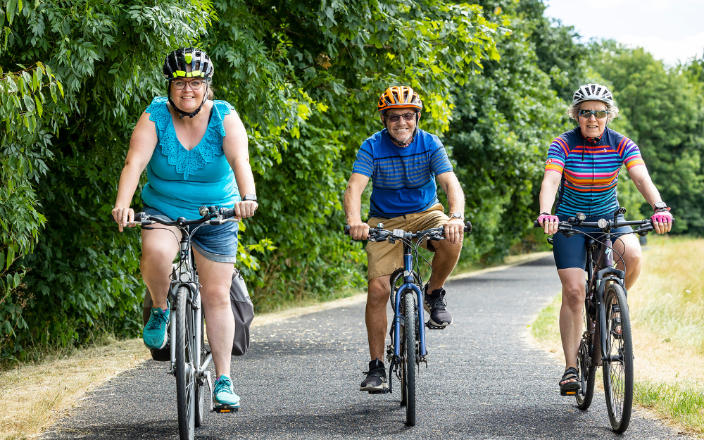 Three casually dressed cyclists ride towards the camera on a cycle path