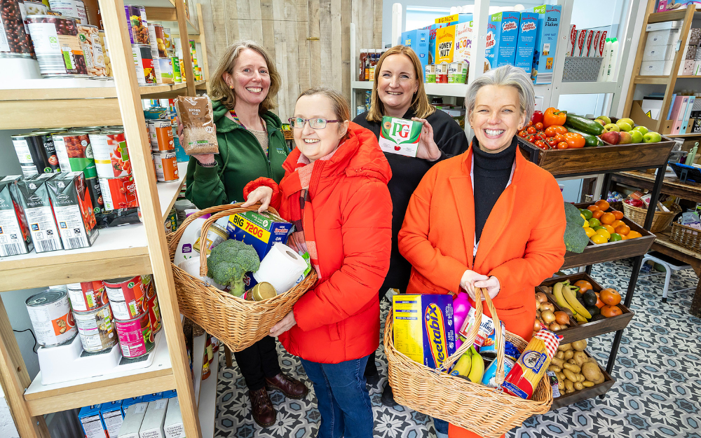 Opening of roots community pantry, people involved smile to the camera holding baskets of fresh food and other items