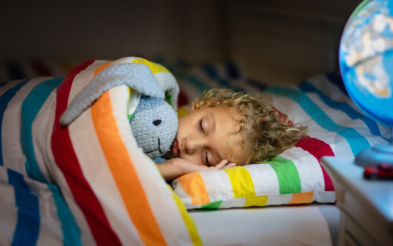 A boy sleeping in bed with a cuddly rabbit, next to a light up globe lamp