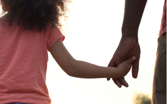 A child with their arm out, holding their parent or carer's hand