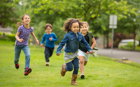 Four children smiling and running across the grass together