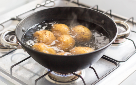 A pan of potatoes in boiling water on a gas hob