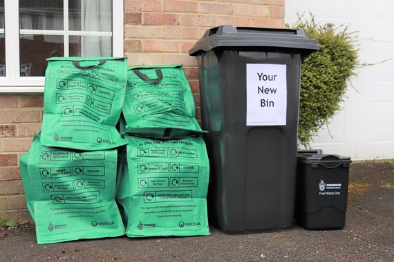 Four green recycling bags, a black recycling bin with a sign saying "your new bin" and a food waste bin outside a house