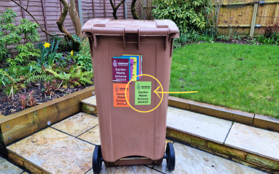 A Wokingham Borough Council brown garden waste bin with stickers of different colours