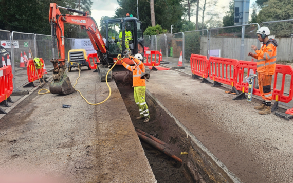 Workers in high viz use a digger to excavate part of the road