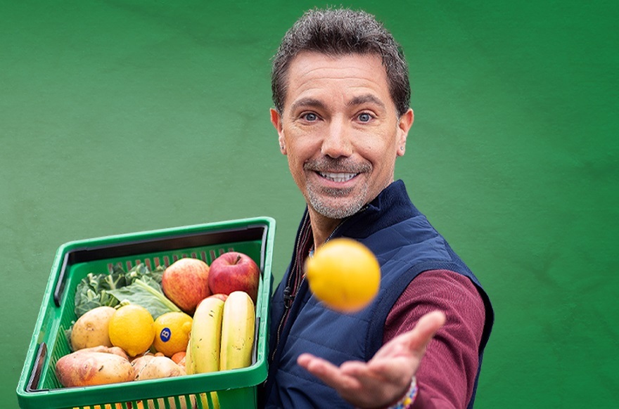 Photo of celebrity chef Gino D'Acampo holding a basket of fresh fruit and vegetables while throwing a lemon towards the camera