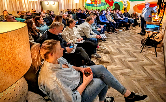 Rows of people sitting in chairs and watching a presentation in a relaxed, informal meeting room