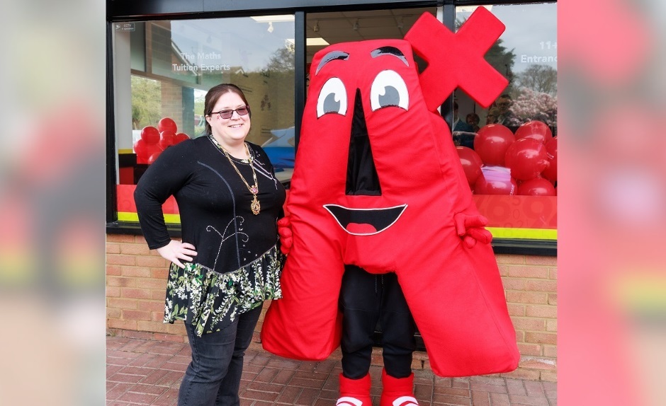 A woman smiling outside the Mathnasium town centre retail unit with a mascot dressed as a giant A+ grade
