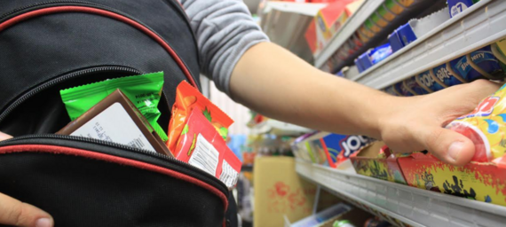 Stock photograph of a shoplifter's hands stuffing chocolate bars from the shelves into a small purse