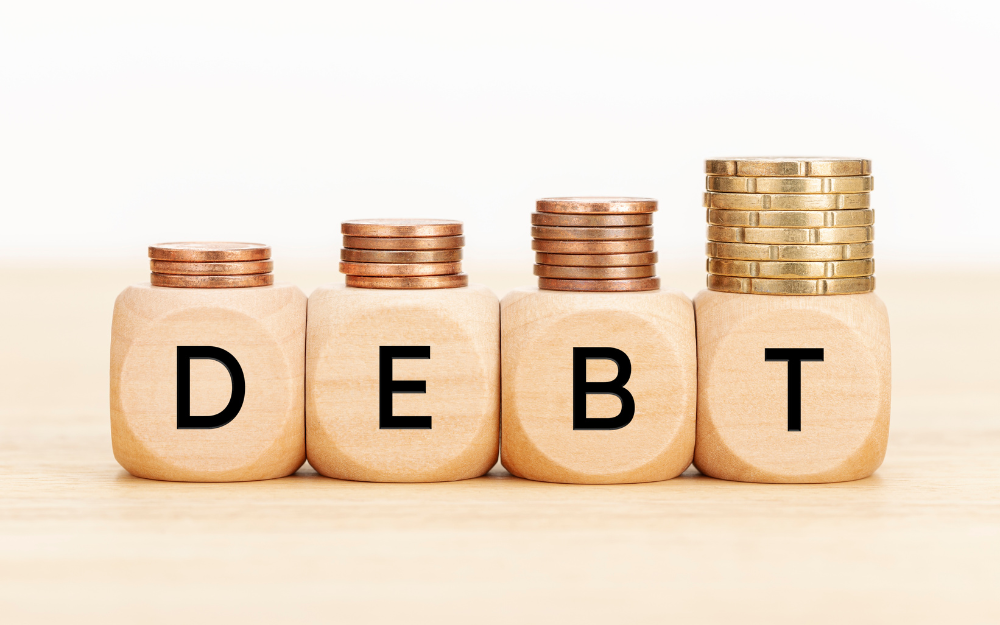 Cubes spelling debt with increasing large stacks of coins on top of each letter cube