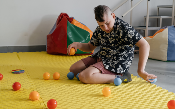 A teenage boy knelt on a soft mat, rolling colourful balls