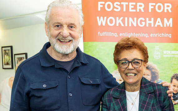 Havva and Jim smile to the camera in front of a 'foster for Wokingham' banner