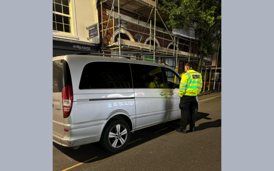 A police officer speaking to a taxi driver through the vehicle window at a taxi rank in Wokingham town centre