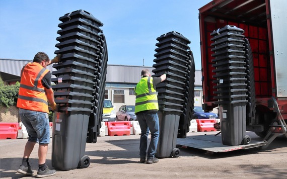 Contractors loading stacks of wheeled bins to the back of a vehicle