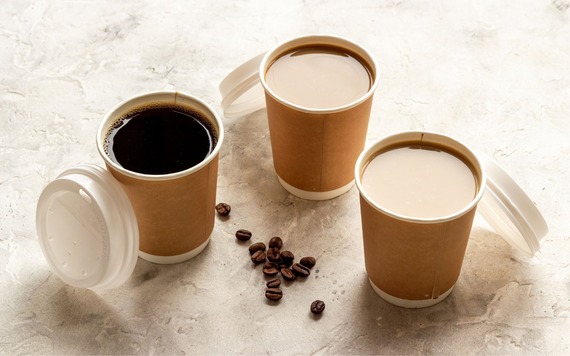 A top view of three paper coffee cups with lids on their side and some coffee beans