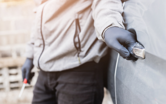 Person with black latex gloves breaks into a van using a tool