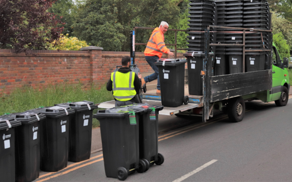 Black wheeled rubbish bins being unloaded from a truck