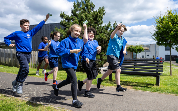 Six children in Addington school uniforms run along a path holding their beat the street cards aloft