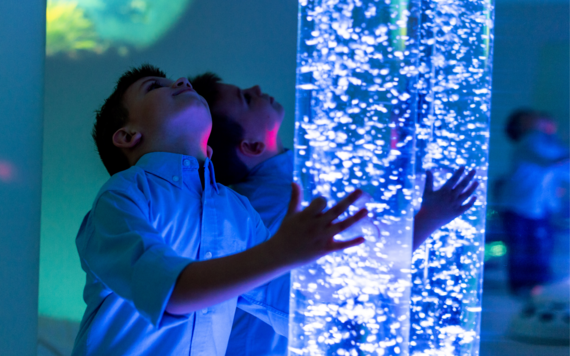 A child holding onto a glowing, blue sensory tube with bubbles inside