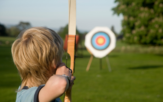 A child holding a bow and arrow and aiming for a target