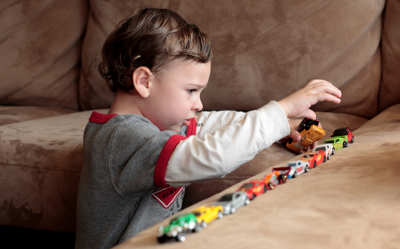 A young child lines up toy cars on a sofa