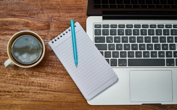 A cup of coffee, notebook and laptop on top of a table