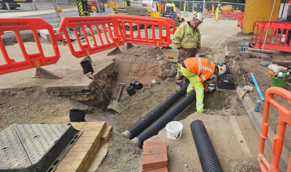 workers in high viz laying ductwork beneath ground level at California Cross