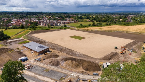An aerial photo of new sports pitches being dug up and laid, and a single-storey pavilion under construction