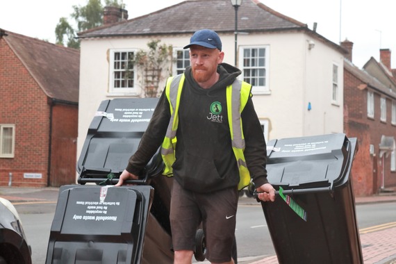 a bin delivery man wearing a baseball cap wheels four black bins through Wokingham town centre