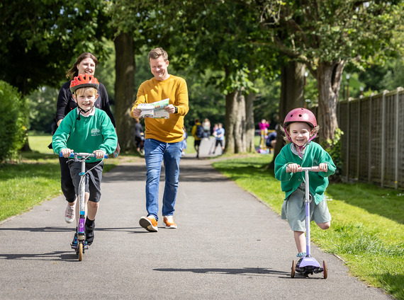 Two adults walking and two children scooting